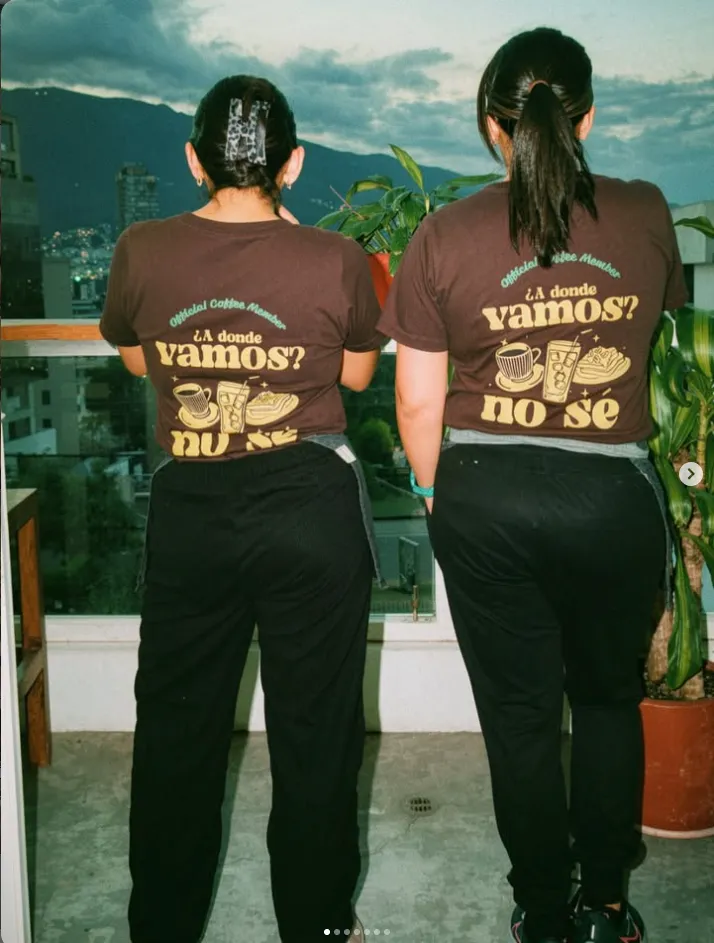 Dos integrantes del equipo de espaldas con camisetas de '¿A dónde vamos? No sé' frente a las montañas de Quito