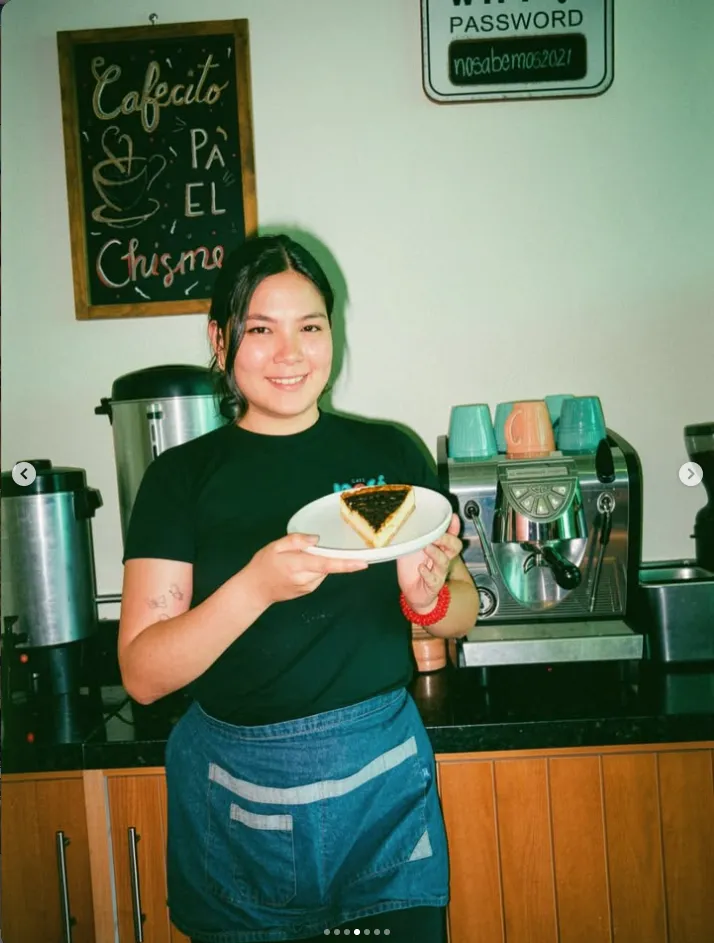 Integrante del equipo sonriendo con un postre en la mano junto a la máquina de espresso