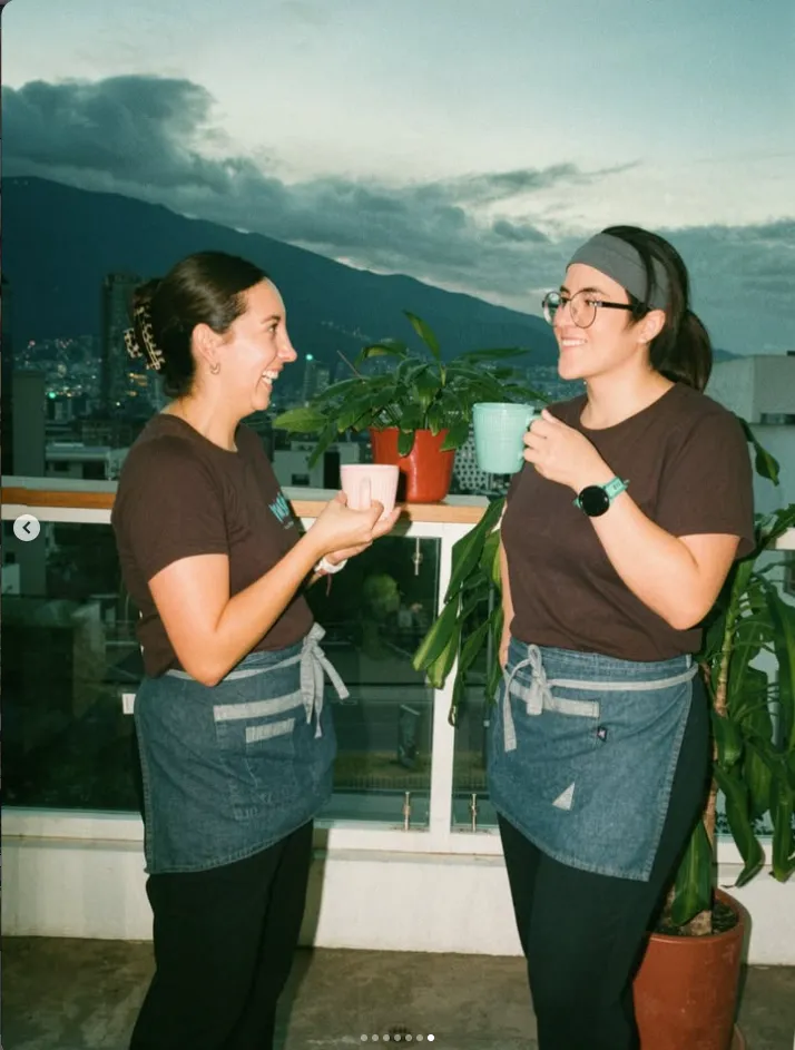 Dos compañeras brindando con tazas en la terraza con vista a la ciudad